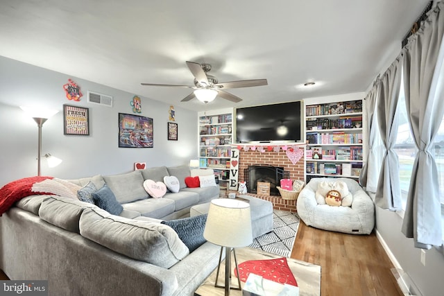 living room with ceiling fan, wood-type flooring, a fireplace, and built in features