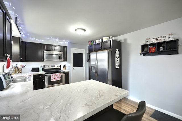 kitchen featuring appliances with stainless steel finishes, hardwood / wood-style floors, a kitchen breakfast bar, and kitchen peninsula