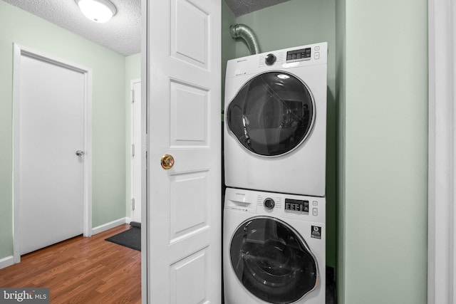 laundry room featuring stacked washer and dryer, hardwood / wood-style floors, and a textured ceiling