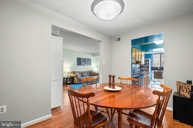 dining space with sink, a textured ceiling, and light hardwood / wood-style flooring