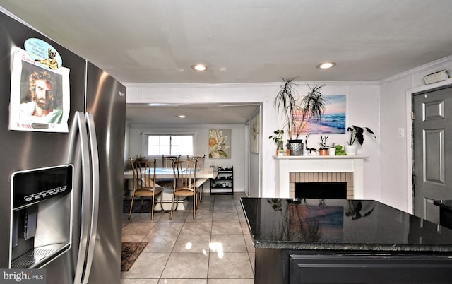 kitchen featuring dark stone counters, ornamental molding, light tile patterned floors, stainless steel fridge with ice dispenser, and a brick fireplace