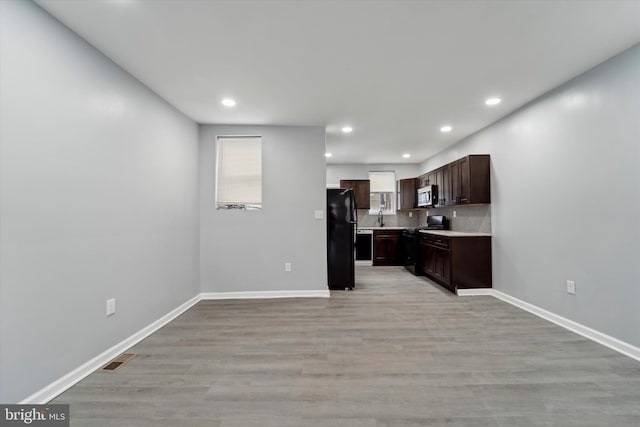 kitchen with black refrigerator, tasteful backsplash, sink, stove, and light hardwood / wood-style flooring