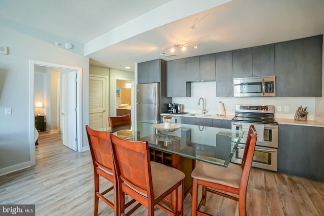 kitchen featuring appliances with stainless steel finishes, sink, a breakfast bar, and light hardwood / wood-style flooring