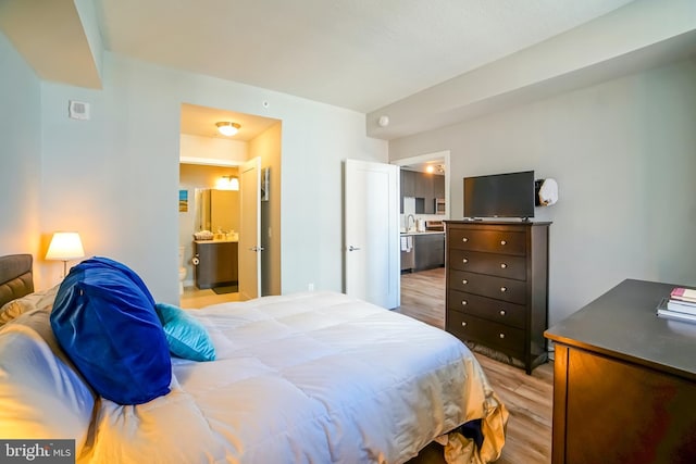 bedroom featuring sink, ensuite bath, and light wood-type flooring