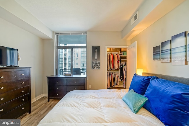 bedroom with a walk in closet, light wood-type flooring, and a closet