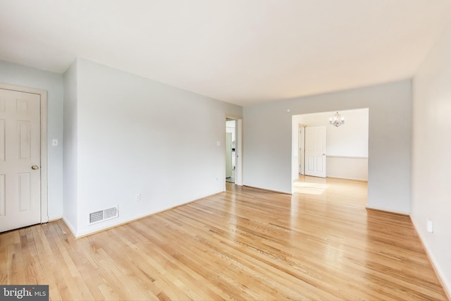 spare room with an inviting chandelier and light hardwood / wood-style floors