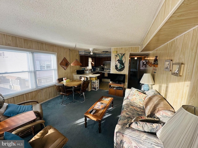 living room with ceiling fan, carpet floors, a textured ceiling, and wood walls