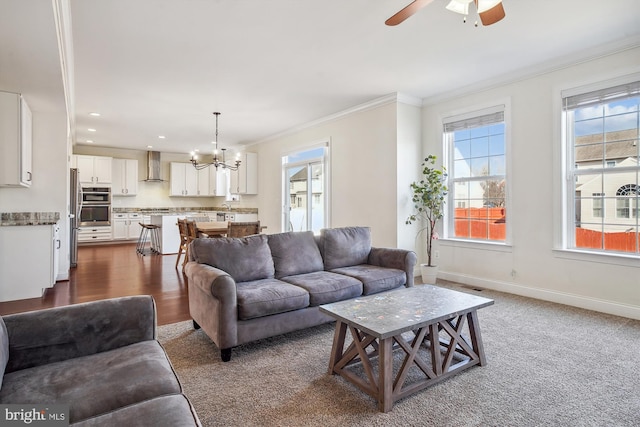 living room featuring dark carpet, sink, ceiling fan with notable chandelier, and ornamental molding