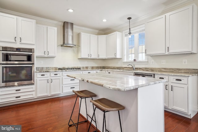 kitchen with wall chimney range hood, white cabinetry, hanging light fixtures, light stone counters, and a kitchen island