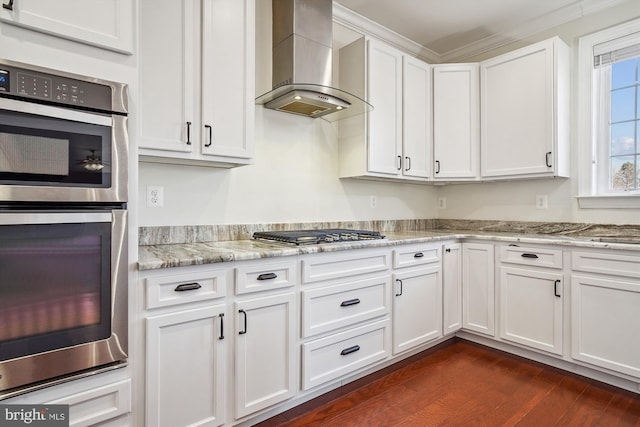 kitchen with appliances with stainless steel finishes, dark hardwood / wood-style floors, white cabinets, light stone countertops, and wall chimney range hood