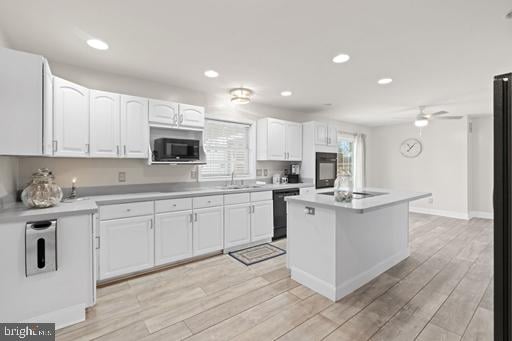 kitchen featuring white cabinetry, light wood-type flooring, black appliances, and a kitchen island