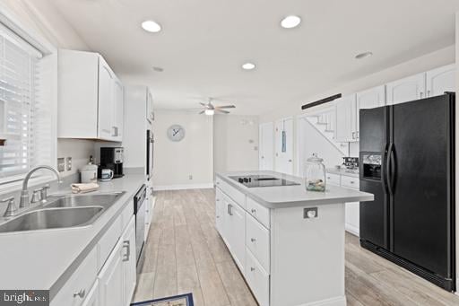 kitchen featuring sink, white cabinets, a center island, black appliances, and light wood-type flooring