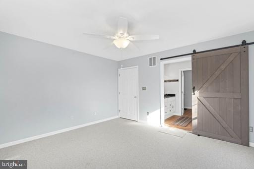 unfurnished bedroom with ceiling fan, a barn door, and carpet