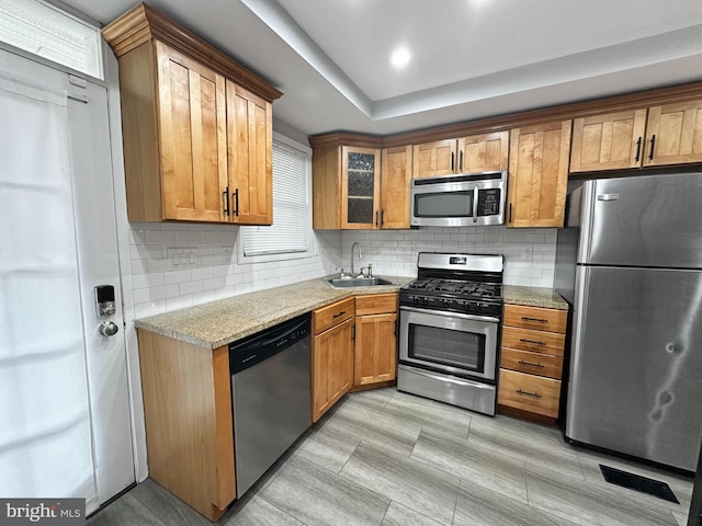 kitchen with sink, decorative backsplash, stainless steel appliances, and light stone countertops