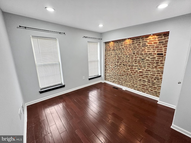 unfurnished room featuring brick wall and hardwood / wood-style floors