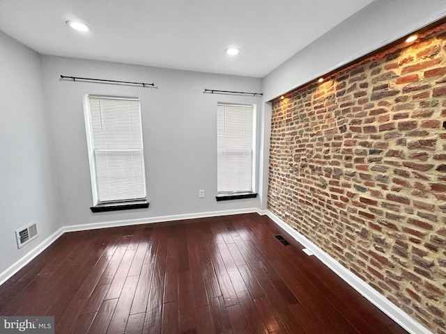 unfurnished room featuring brick wall and dark hardwood / wood-style floors