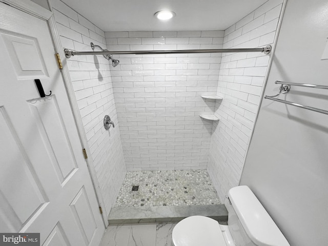 bathroom with a tile shower and toilet