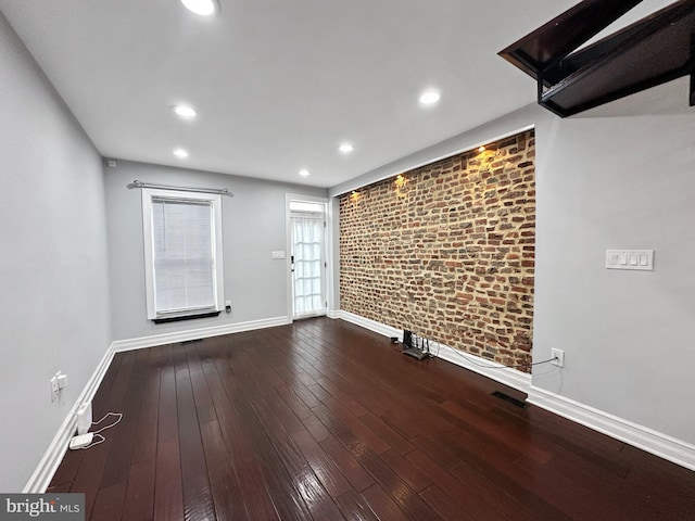 unfurnished room with hardwood / wood-style flooring and brick wall