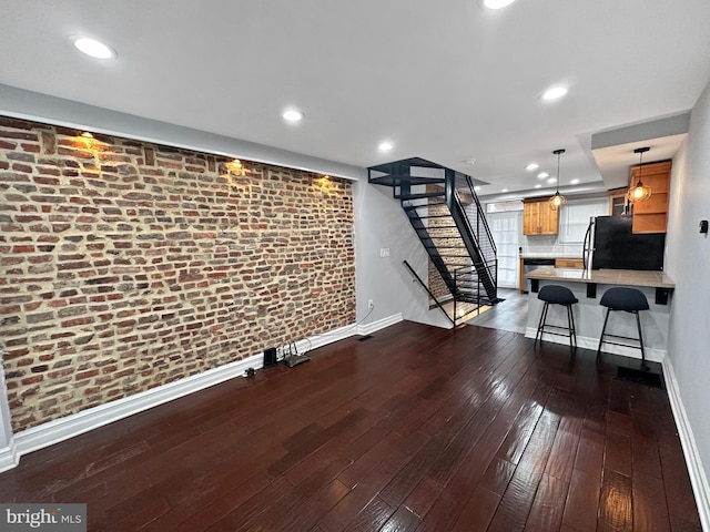 unfurnished living room with brick wall and dark wood-type flooring