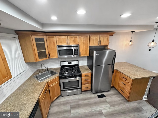 kitchen with sink, light stone counters, hanging light fixtures, stainless steel appliances, and decorative backsplash