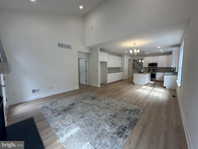 unfurnished living room featuring a notable chandelier, a towering ceiling, light hardwood / wood-style flooring, and sink