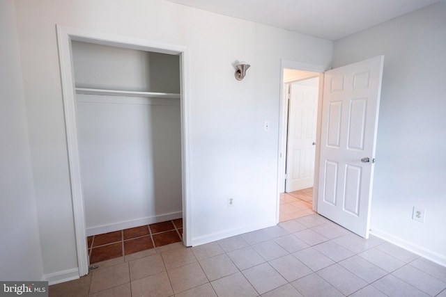 unfurnished bedroom featuring light tile patterned floors, baseboards, and a closet