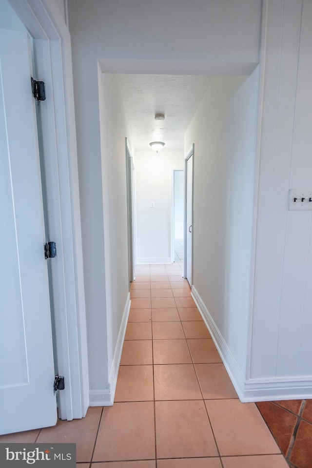 hall featuring light tile patterned flooring and baseboards