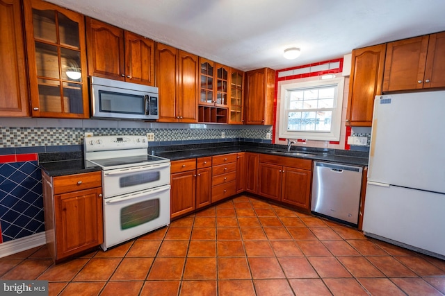 kitchen featuring tile patterned floors, brown cabinets, a sink, dark countertops, and appliances with stainless steel finishes