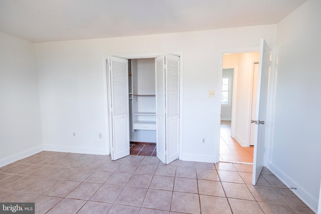 unfurnished bedroom with light tile patterned floors, a closet, and baseboards