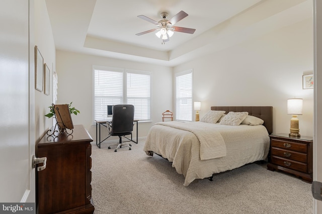 carpeted bedroom with ceiling fan and a raised ceiling