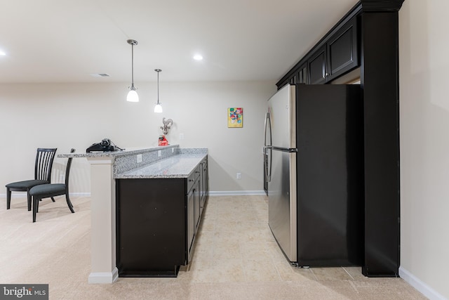 kitchen featuring pendant lighting, light stone countertops, stainless steel refrigerator, and kitchen peninsula