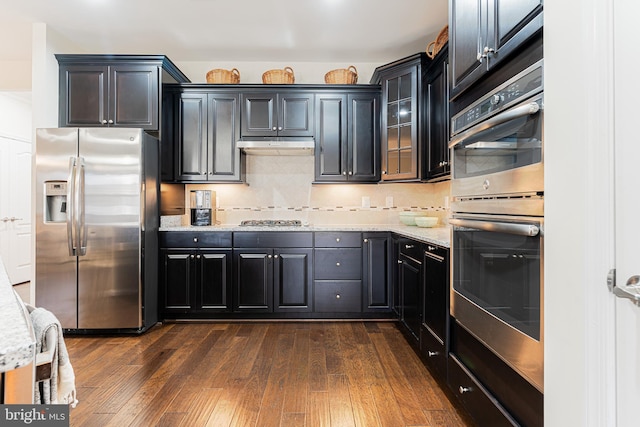 kitchen featuring light stone counters, dark hardwood / wood-style flooring, tasteful backsplash, and appliances with stainless steel finishes