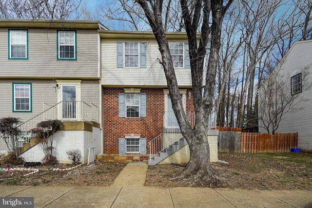 view of front of home featuring stairs, brick siding, and fence