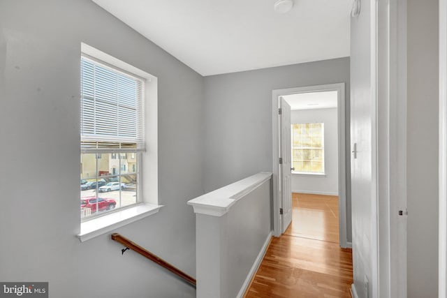 hallway with light wood-type flooring, plenty of natural light, baseboards, and an upstairs landing