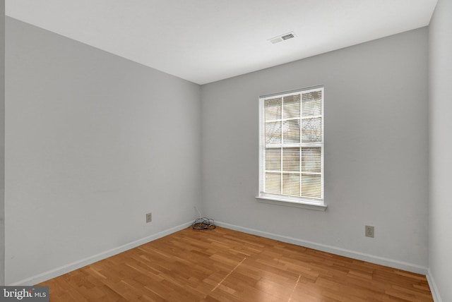 empty room featuring light wood-style flooring, visible vents, and baseboards