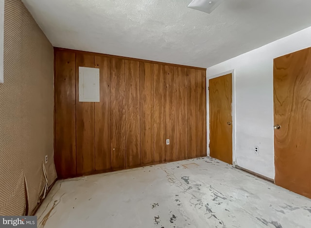 unfurnished room featuring wooden walls, electric panel, and a textured ceiling