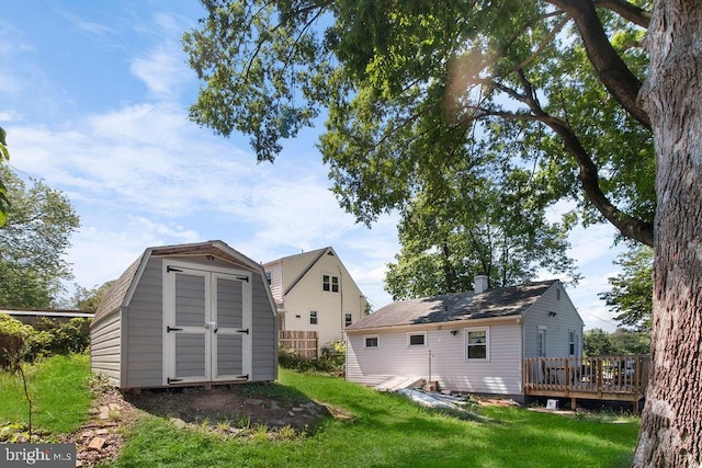 back of property with a deck, a lawn, and a storage unit