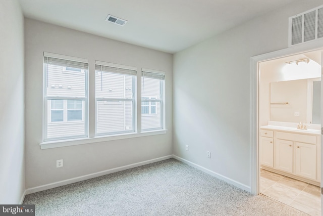 unfurnished bedroom with multiple windows, sink, connected bathroom, and light colored carpet