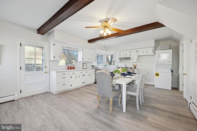 dining room with baseboard heating, stacked washing maching and dryer, beam ceiling, and light hardwood / wood-style flooring