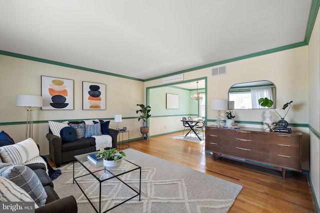 living room featuring a notable chandelier, ornamental molding, and light wood-type flooring