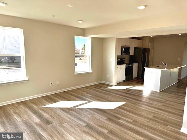 unfurnished living room with sink, plenty of natural light, and light wood-type flooring