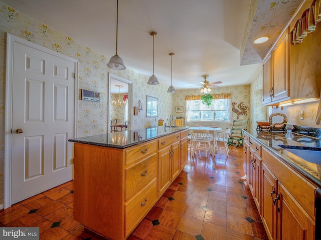 kitchen with pendant lighting, sink, ceiling fan, dark stone countertops, and a center island