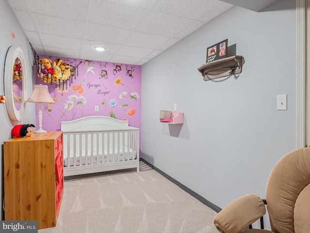 bedroom with a drop ceiling, a nursery area, and carpet flooring