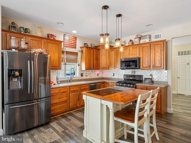 kitchen featuring pendant lighting, sink, backsplash, stainless steel appliances, and a center island