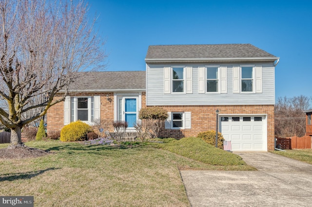 split level home featuring driveway, a shingled roof, a front yard, an attached garage, and brick siding