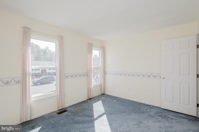 empty room featuring baseboards, visible vents, dark colored carpet, and wainscoting