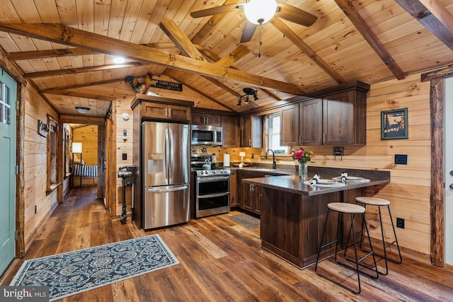 kitchen featuring dark wood-type flooring, appliances with stainless steel finishes, wooden walls, a kitchen bar, and kitchen peninsula