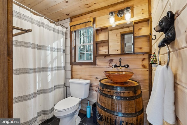 bathroom with toilet, sink, wood walls, wooden ceiling, and tile patterned flooring