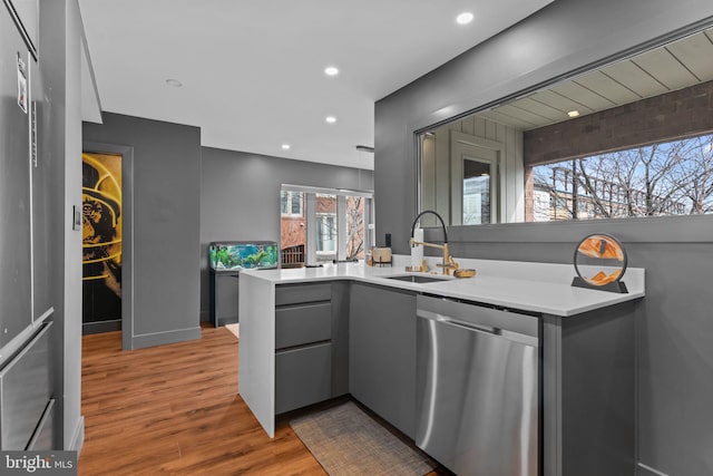 kitchen with gray cabinets, wood-type flooring, sink, stainless steel dishwasher, and kitchen peninsula