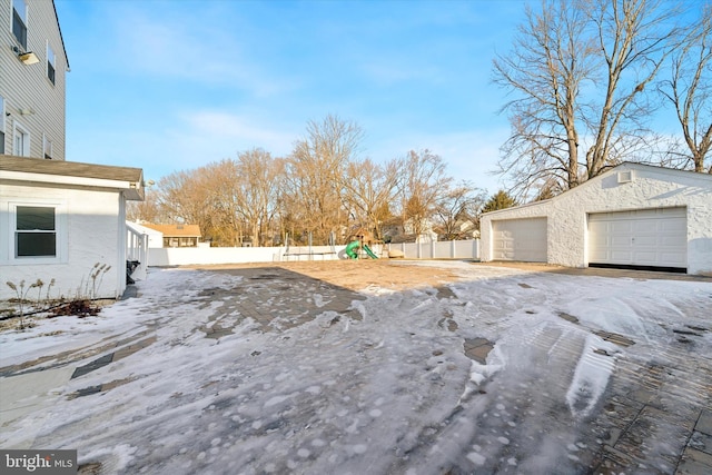 snowy yard with a garage, an outbuilding, and a playground